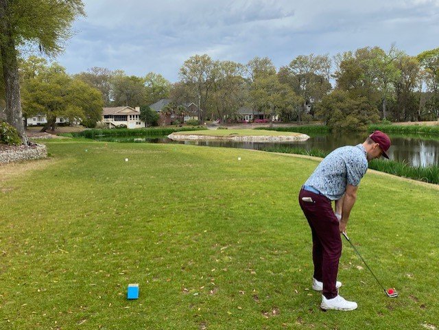 Golfer teeing off toward the island green at Oyster Bay Golf Links Sunset Beach NC