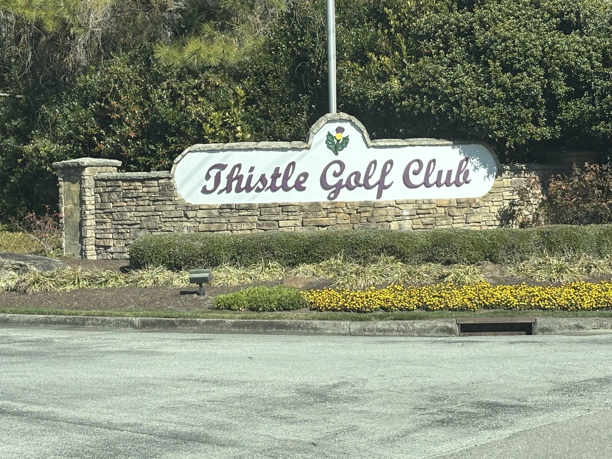 Thistle Golf Club stone entrance sign with yellow flowers in Sunset Beach NC